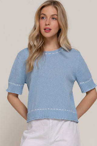 Woman wearing a light blue knit top with white trim on a plain background