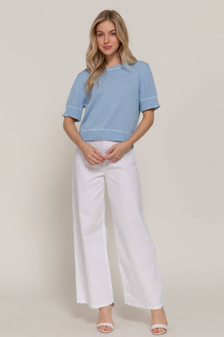 Woman wearing a light blue top and white pants against a plain background