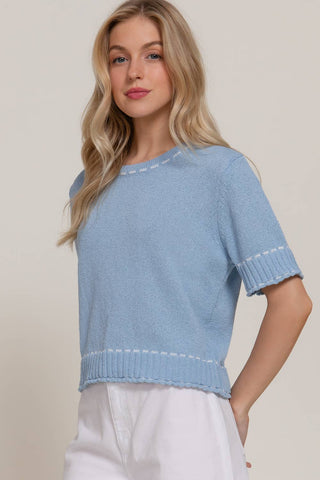 Woman wearing a light blue knit top against a beige background
