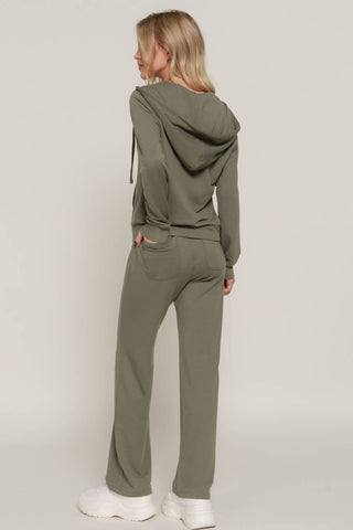 A woman wearing an olive green matching loungewear set, consisting of a cropped hoodie and wide-leg sweatpants, shown from a rear three-quarter view against a light gray studio background.