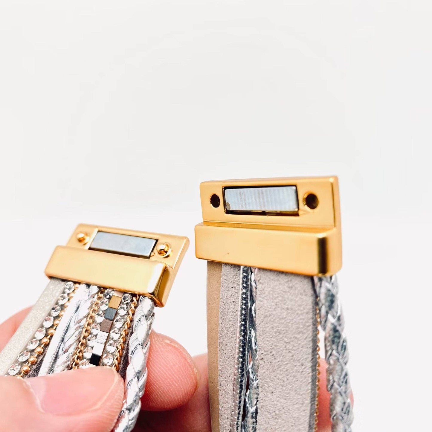 Close-up of two gold clasp bracelets with textured bands on a light gray background