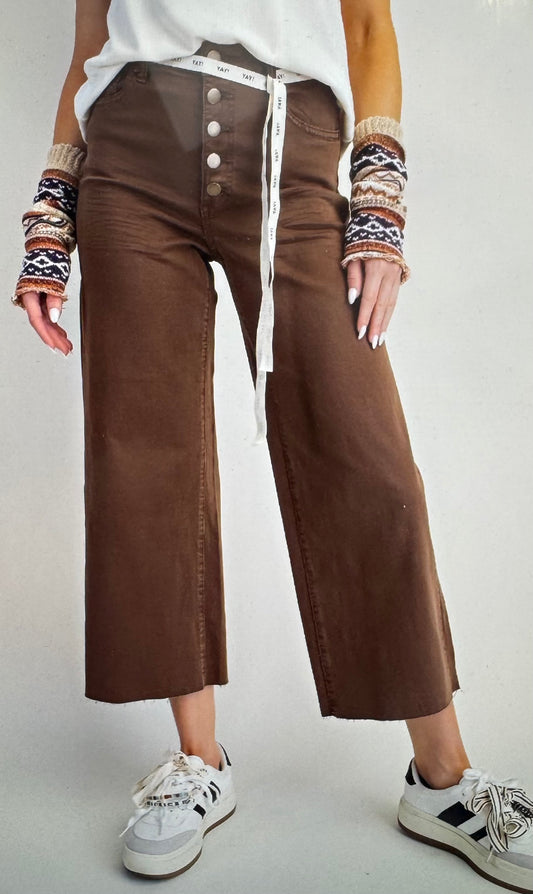 Person wearing brown wide-leg pants with a white top and patterned sleeves on a plain background