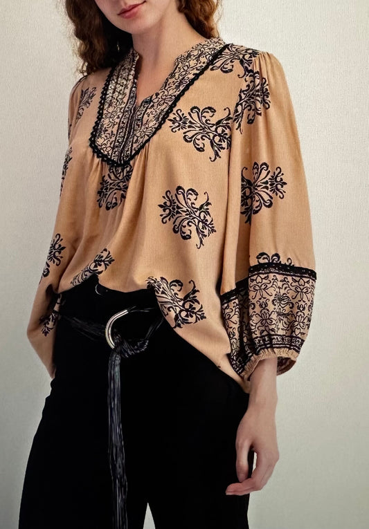 Beige blouse with black intricate patterns worn by a person against a neutral background
