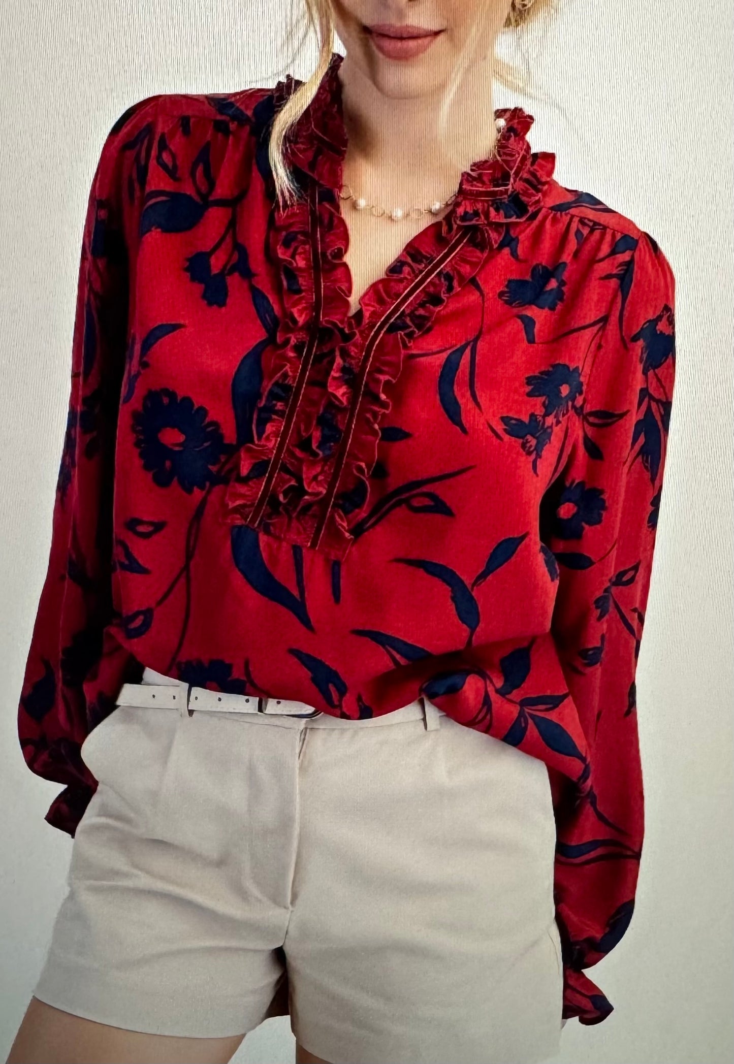 Red floral blouse with ruffled details worn by a person on a plain background