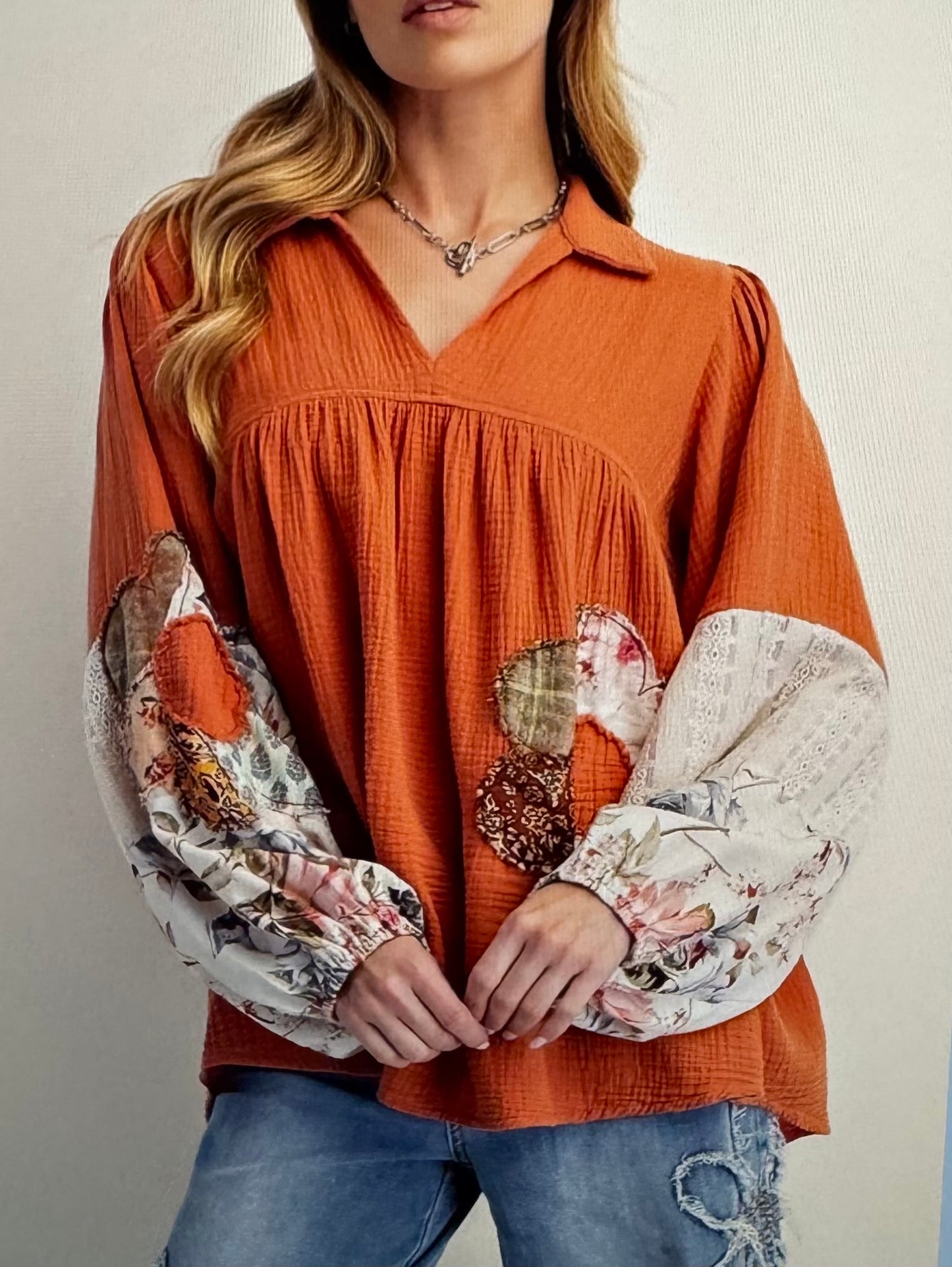 Person wearing an orange blouse with floral sleeves against a neutral background