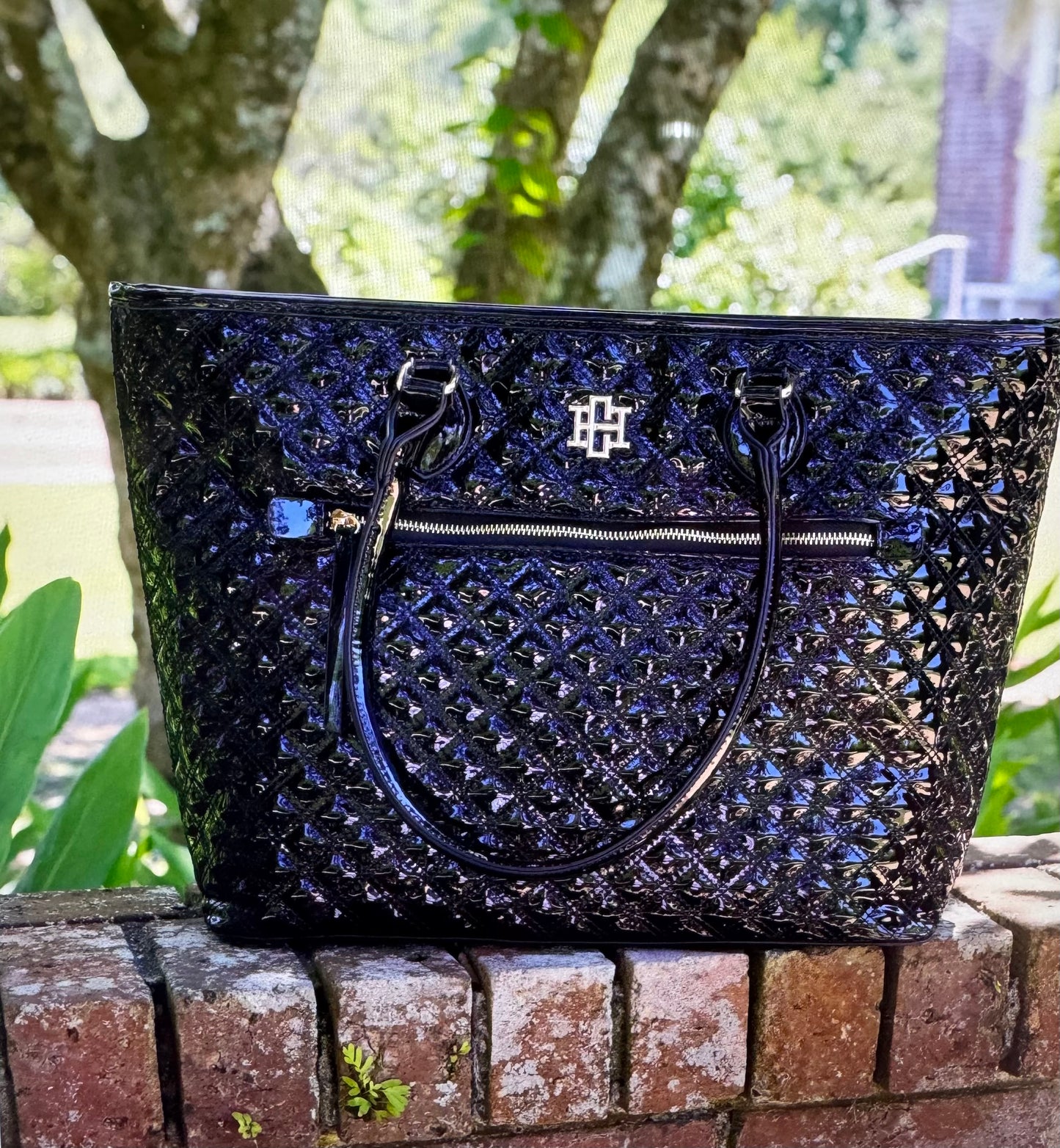 Black textured handbag with a brand logo on a brick ledge outdoors