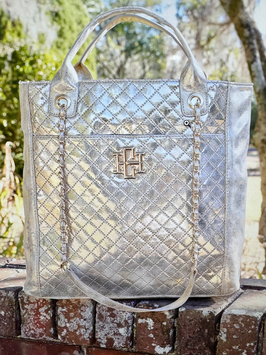 Silver quilted handbag with a brand logo on a wooden surface with a blurred natural background