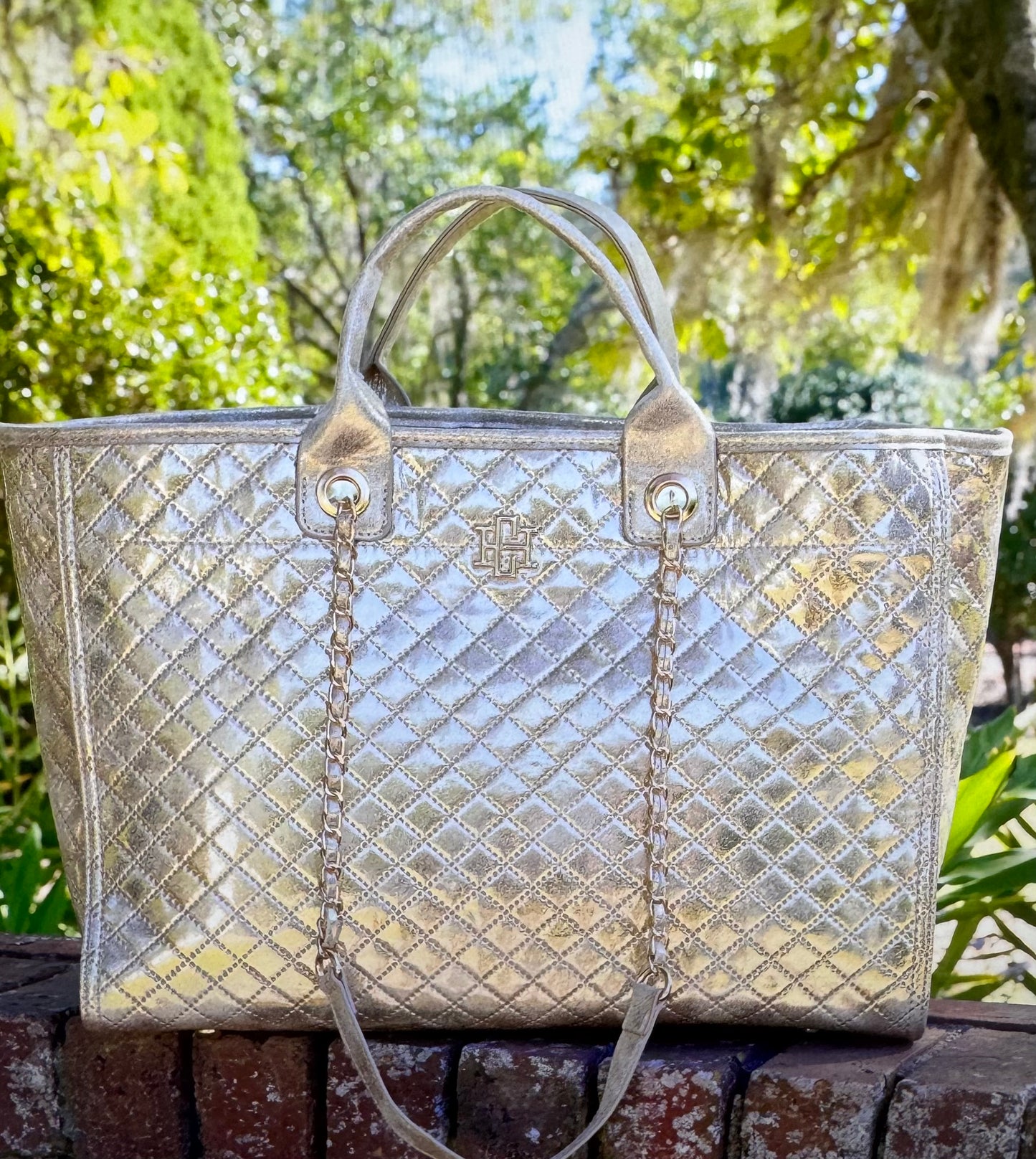 Silver quilted handbag on a wooden surface with greenery in the background