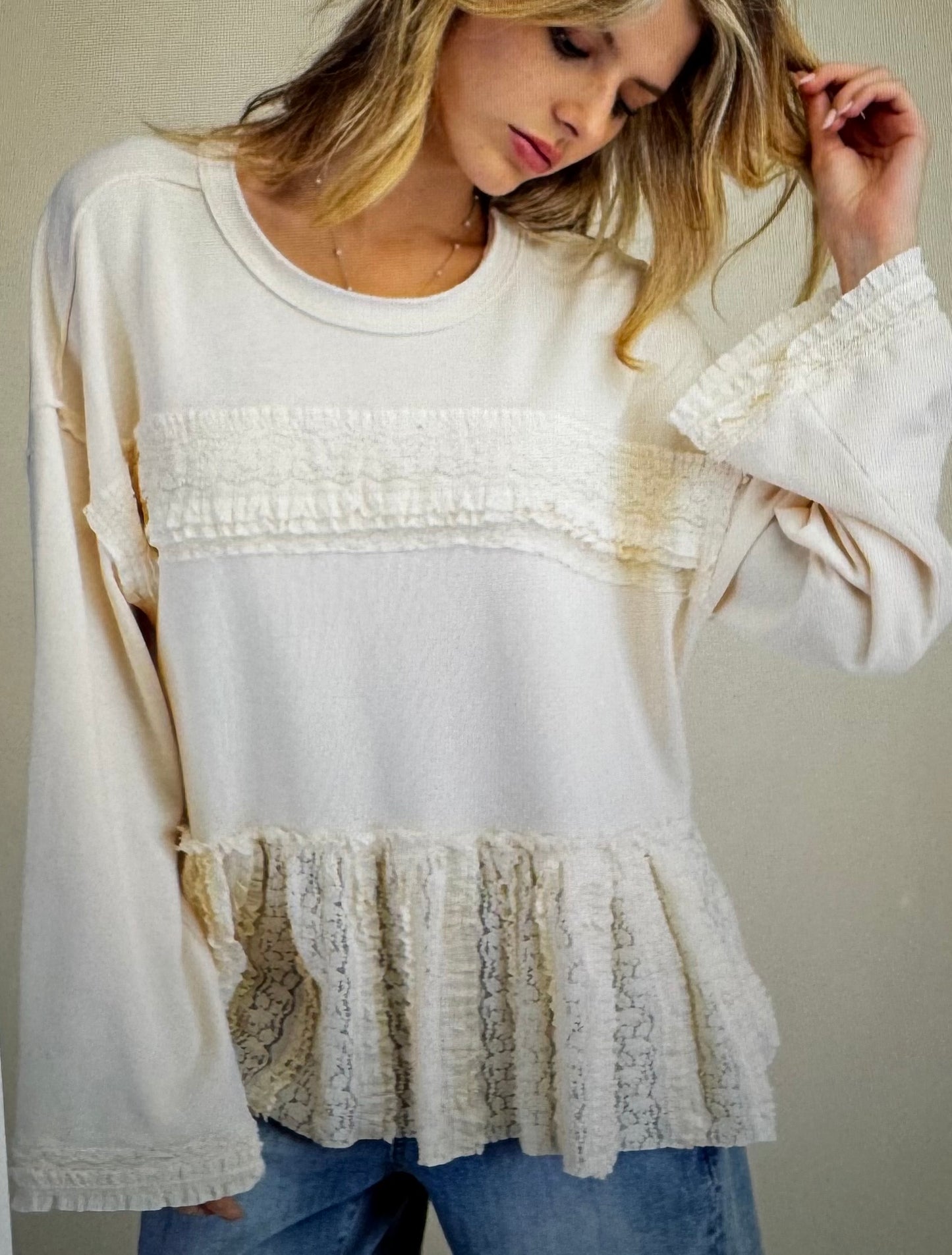 Woman wearing a white blouse with ruffled details and blue jeans against a plain background