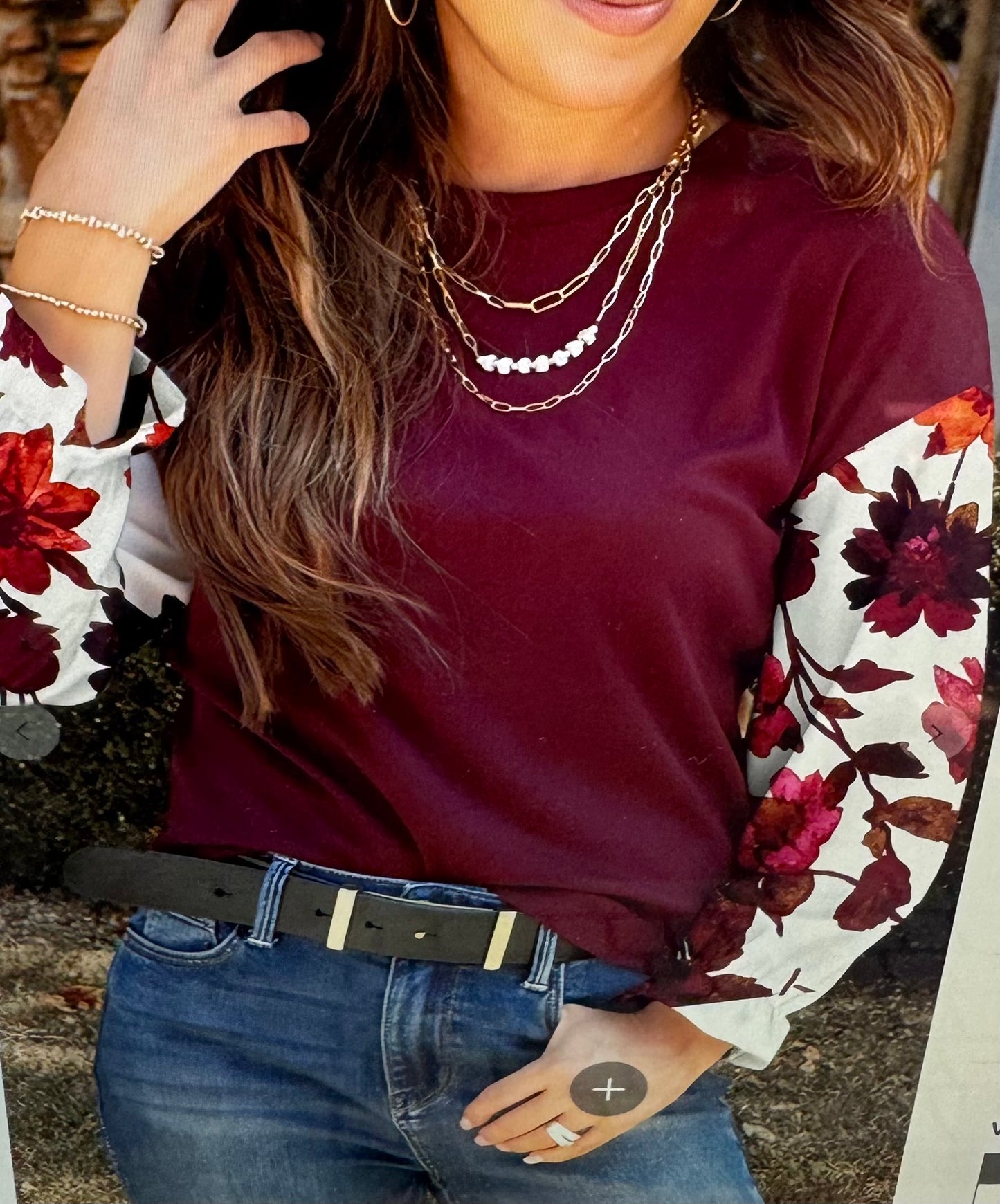 Woman wearing a burgundy sweater with floral sleeves and jeans, standing outdoors.