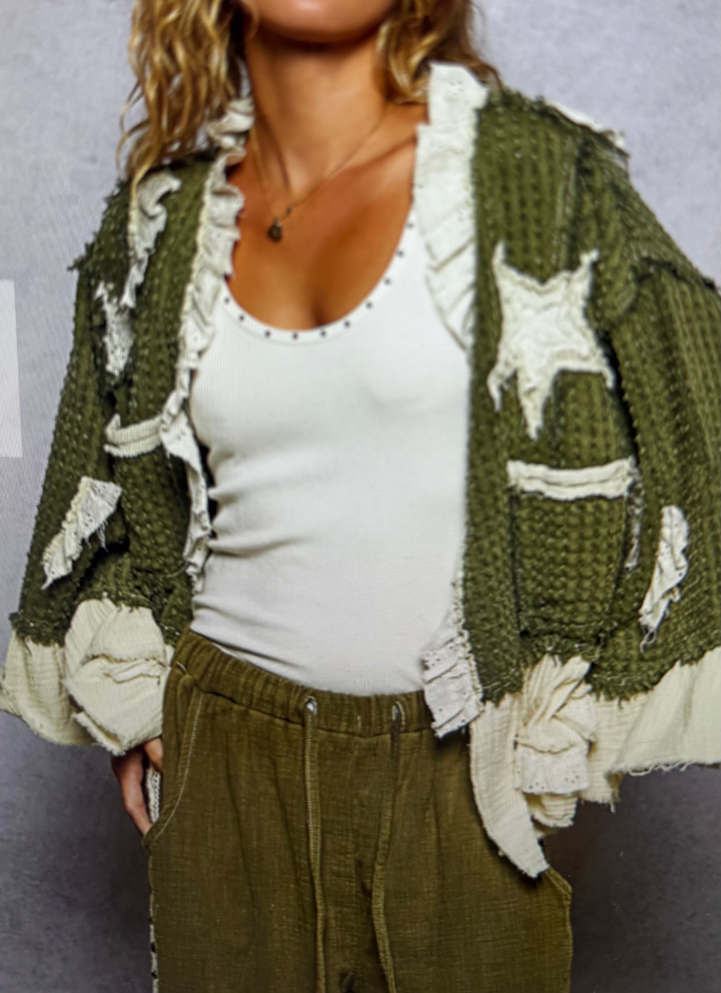 Person wearing a green textured cardigan over a white top and green pants against a plain background