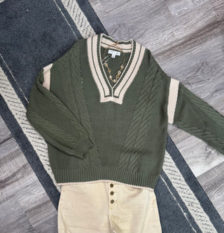 Long sleeve V Neck Cable Pullover  Green sweater with beige contrast details on a gray rug with a pair of Button pants
