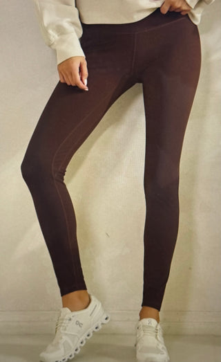 Model in brown leggings standing in front of light colored wall