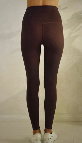 Model showing the backside of brown leggings standing in front of a light color colored wall
